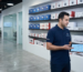 Inside a modern high-tech security showroom. Shelves are neatly stocked with Hikvision boxes and white network switches. A professional engineer in a branded polo shirt is holding a tablet, showing a floor plan to a business client. Bright lighting, clean composition, representing 'best cctv dealers in dubai